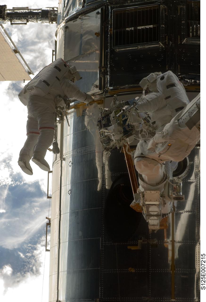 S125-E-007215 (14 May 2009) --- What appears to be a number of astronauts, because of the shiny mirror-like surface of the temporarily-captured Hubble Space Telescope, is actually only two -- astronauts John Grunsfeld (left) and Andrew Feustel. The mission specialists are performing the first of five STS-125 spacewalks and the first of three for this duo.