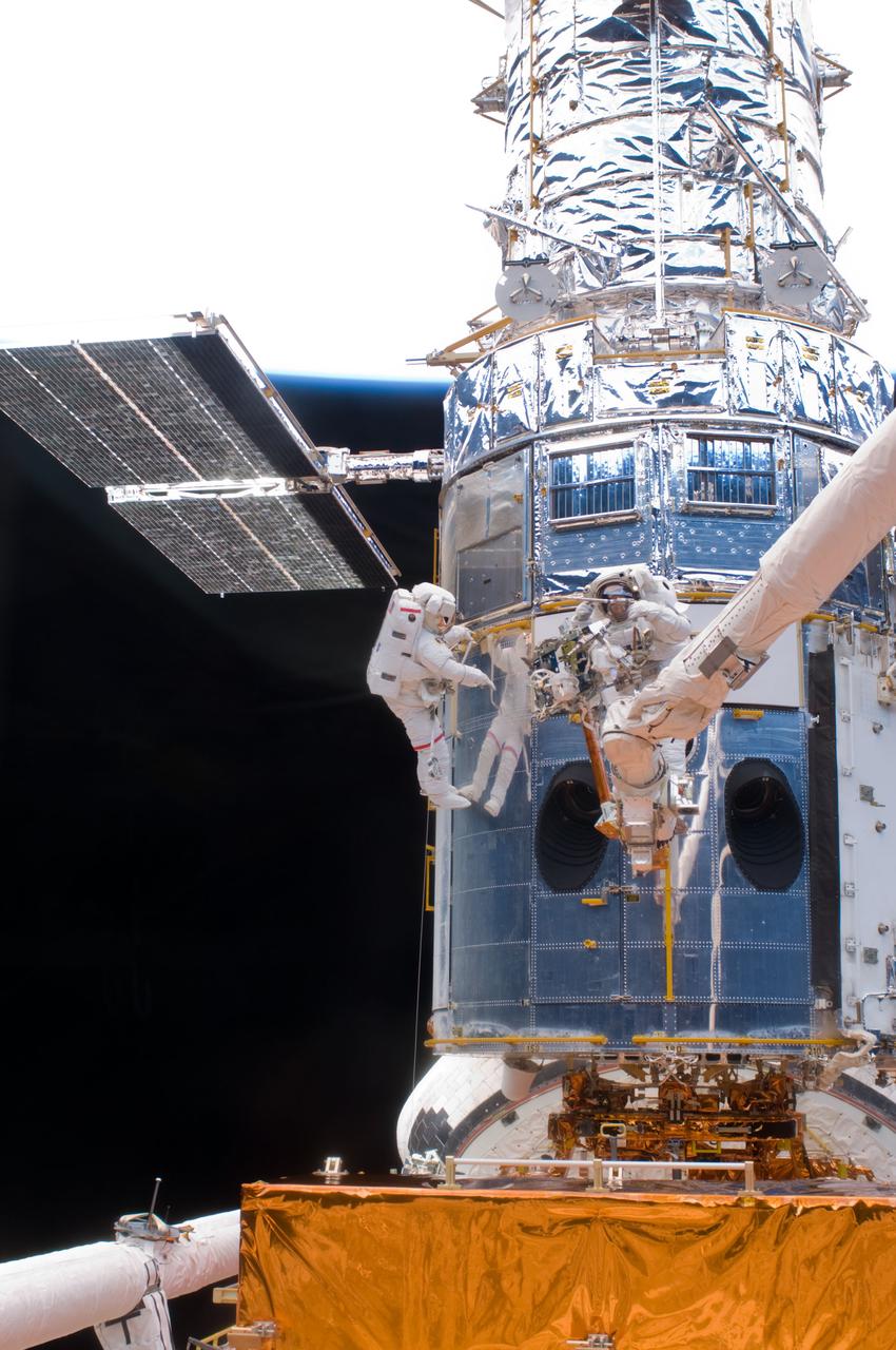 S125-E-007221 (14 May 2009) --- What appears to be a number of astronauts, because of the shiny mirror-like surface of the temporarily-captured Hubble Space Telescope, is actually only two -- astronauts John Grunsfeld (left) and Andrew Feustel. The mission specialists are performing the first of five STS-125 spacewalks and the first of three for this duo.