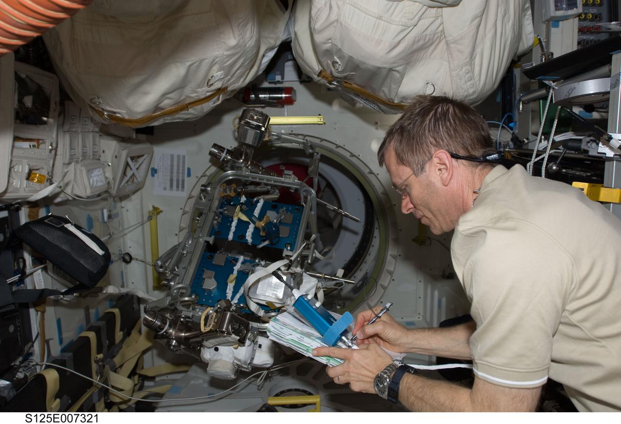S125-E-007321 (14 May 2009) --- Astronaut Gregory C. Johnson, STS-125 pilot, makes notes on a checklist on the middeck of Space Shuttle Atlantis during flight day four activities. Extravehicular activity (EVA) hardware is visible in the background.