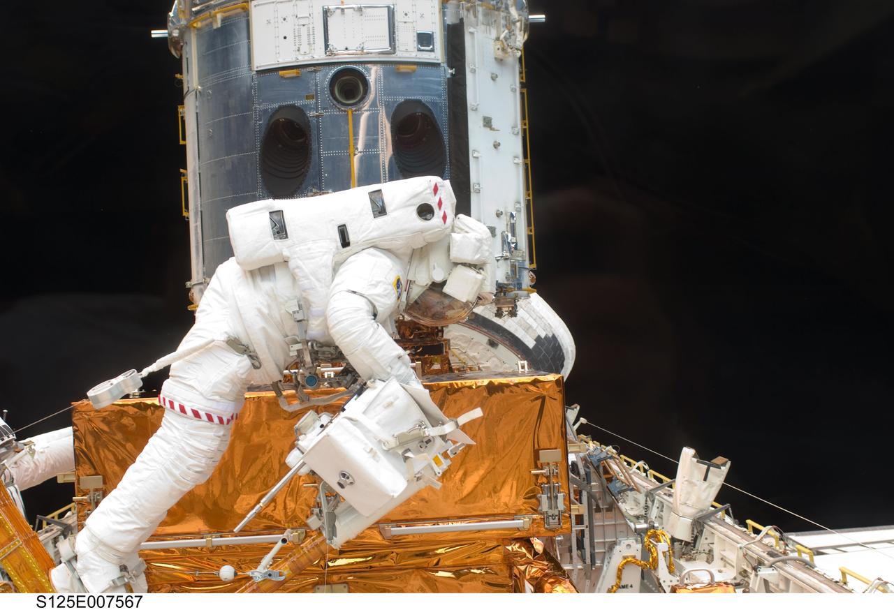 S125-E-007567 (15 May 2009) --- Astronaut Michael Good works with the Hubble Space Telescope in the cargo bay of the Earth-orbiting Space Shuttle Atlantis. Astronauts Good and Mike Massimino (working in background) participated in the second session of STS-125 extravehicular activity -- as part of a five-day beehive-like agenda of spacewalking and work on the giant orbital observatory.