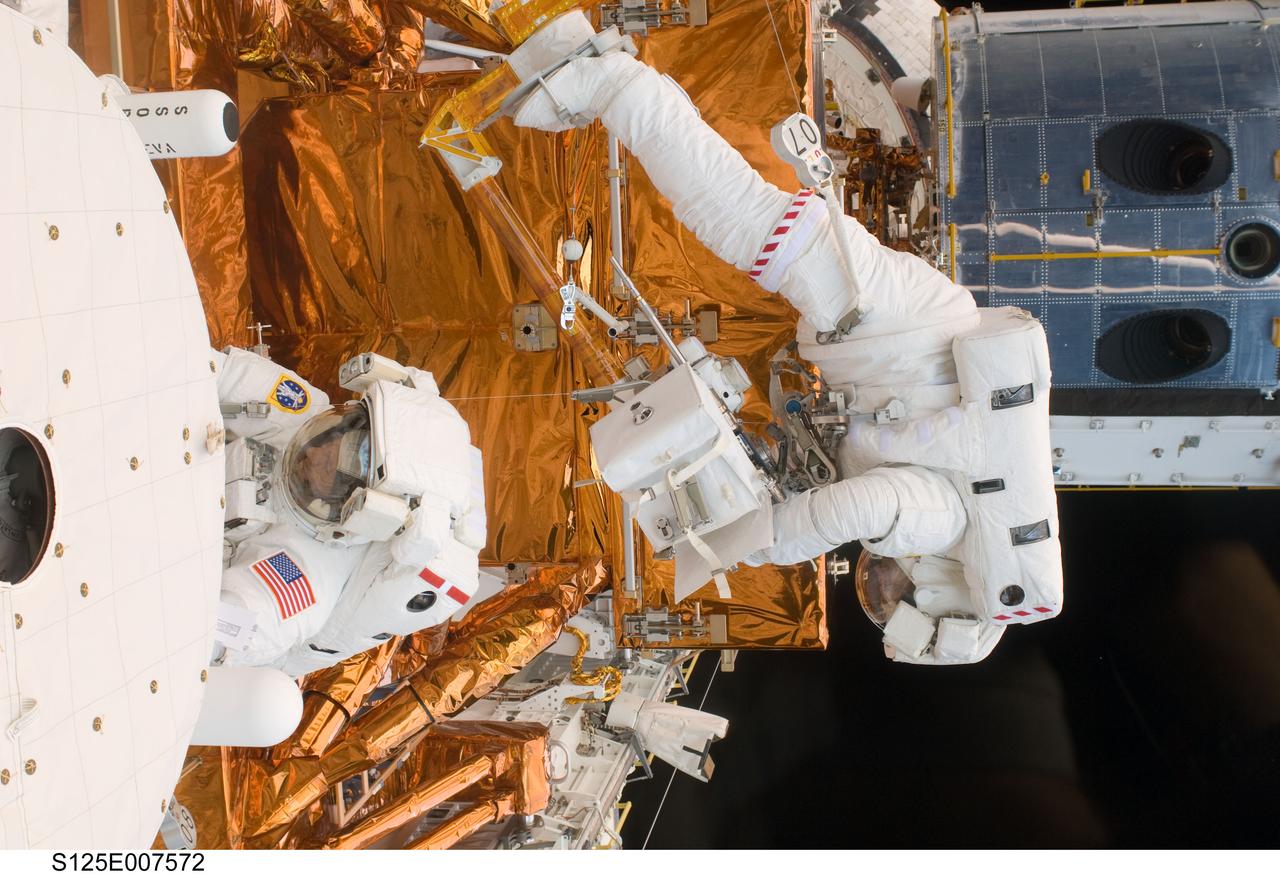 S125-E-007572 (15 May 2009) --- Astronaut Michael Good works with the Hubble Space Telescope in the cargo bay of the Earth-orbiting Space Shuttle Atlantis. Astronauts Good and Mike Massimino (bottom frame) participated in the second session of STS-125 extravehicular activity -- as part of a five-day beehive-like agenda of spacewalking and work on the giant orbital observatory.