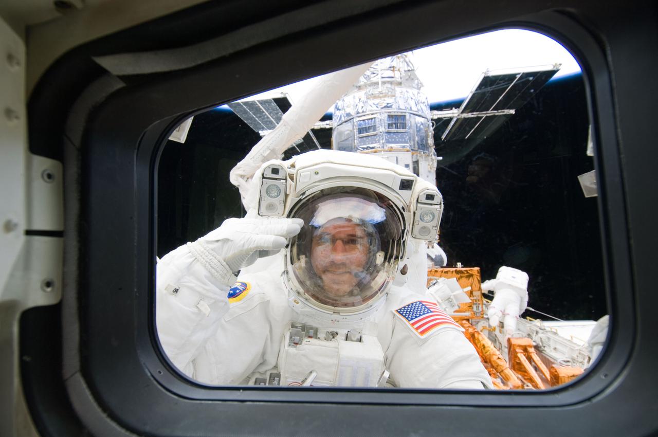 S125-E-007595 (15 May 2009) --- While standing on the end of Atlantis' remote manipulator system arm, astronaut Michael Good, STS-125 mission specialist, pays tribute to his commander and all his crewmates with a military-style salute.  Astronauts Good and Mike Massimino (working in the right background), mission specialist, are continuing work on the Hubble Space Telescope, locked down in the orbiter's cargo bay. After their May 15 tasks were completed, three more sessions of extravehicular activity, on back to back to back days, awaited the seven-person crew.