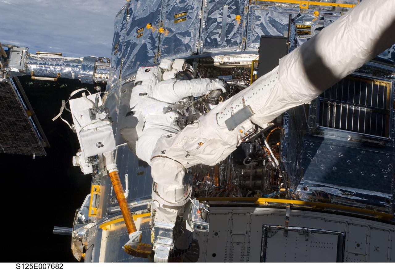 S125-E-007682 (15 May 2009) --- While standing on the end of Atlantis' remote manipulator system arm, astronaut Michael Good, STS-125 mission specialist, uses a power tool to perform work on the Hubble Space Telescope.