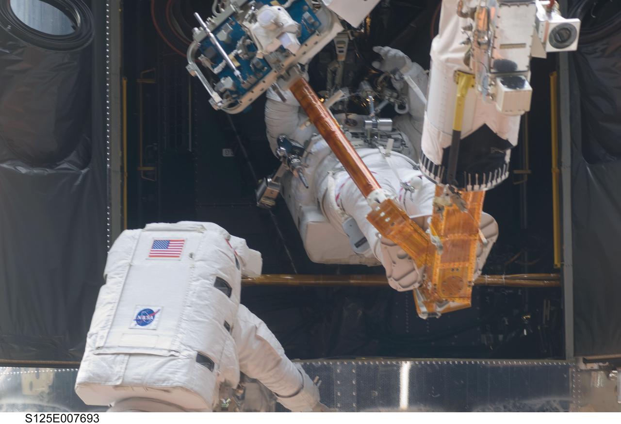 S125-E-007693 (15 May 2009) --- While standing on the end of Atlantis' remote manipulator system arm, astronaut Michael Good (right), STS-125 mission specialist, gives maneuver directions to supportive crewmates inside the shuttle. Good and astronaut Mike Massimino (foreground), mission specialist, continue work on the Hubble Space Telescope, locked down in the orbiter's cargo bay. After their May 15 tasks were completed, three more sessions of extravehicular activity, on back to back to back days, awaited the seven-person crew.