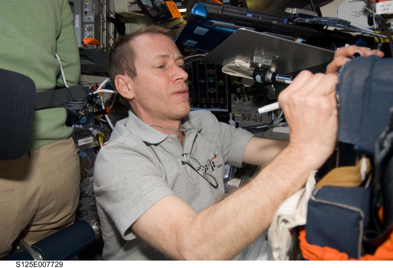 S125-E-007729 (15 May 2009) --- Astronaut Gregory C. Johnson, SS-125 pilot, scribbles a note on Atlantis' flight deck while two of crewmates perform a space walk to work on the Hubble Space Telescope.