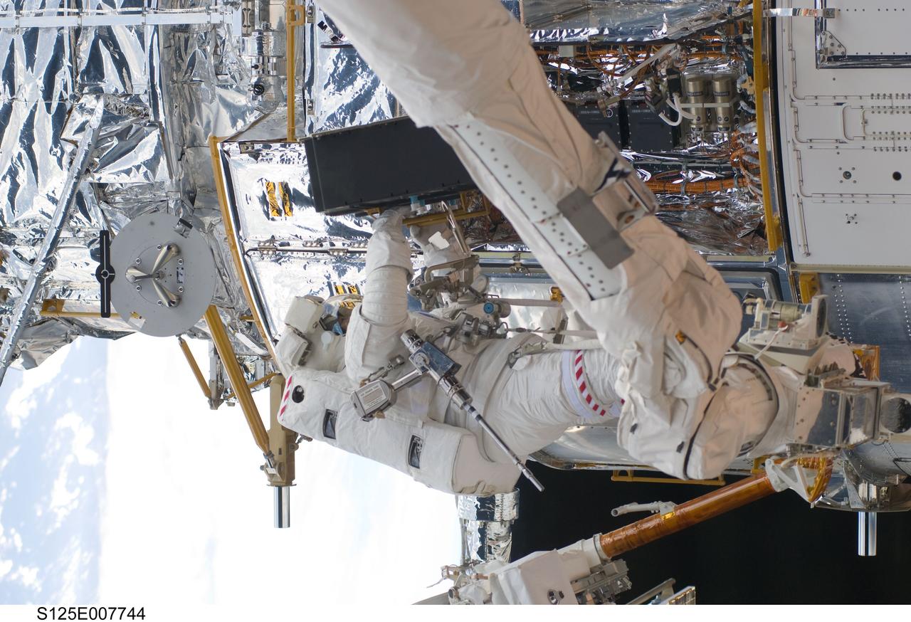 S125-E-007744 (15 May 2009) --- While standing on the end of Atlantis' remote manipulator system arm, astronaut Michael Good, STS-125 mission specialist, works on the Hubble Space Telescope.  Astronauts Good and Mike Massimino (out of frame), mission specialist, continue work on the Hubble Space Telescope, locked down in the orbiter's cargo bay. After their May 15 tasks were completed, three more sessions of extravehicular activity, on back to back to back days, awaited the seven-person crew.
