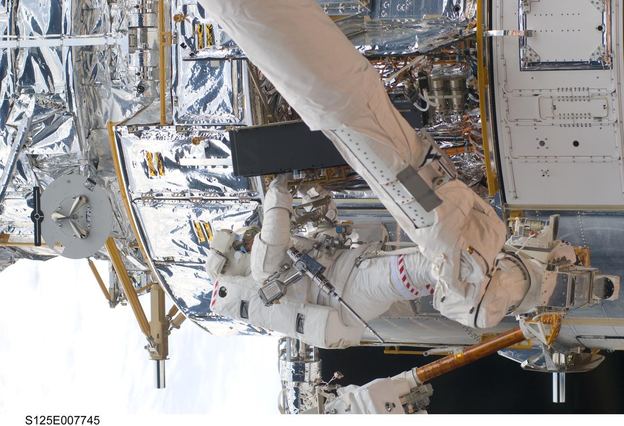 S125-E-007745 (15 May 2009) --- While standing on the end of Atlantis' remote manipulator system arm, astronaut Michael Good, STS-125 mission specialist, works on the Hubble Space Telescope.  Astronauts Good and Mike Massimino (out of frame), mission specialist, continue work on the Hubble Space Telescope, locked down in the orbiter's cargo bay. After their May 15 tasks were completed, three more sessions of extravehicular activity, on back to back to back days, awaited the seven-person crew.