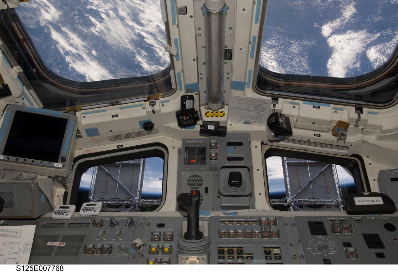 S125-E-007768 (15 May 2009) --- Solar panels on the Hubble Space Telescope make for some unique window shades in this scene photographed from the flight deck of the Earth-orbiting Space Shuttle Atlantis. Just below the "shaded" pair of windows are panels of displays and controls very instrumental in the success of the work being done on the giant observatory.