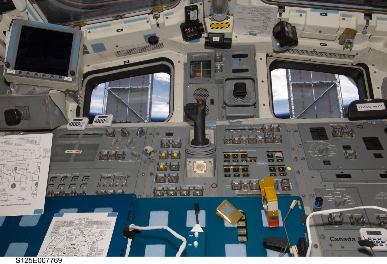 S125-E-007769 (15 May 2009) --- Solar panels on the Hubble Space Telescope make for some unique window shades in this scene photographed from the flight deck of the Earth-orbiting Space Shuttle Atlantis. Just below the "shaded" pair of windows are panels of displays and controls very instrumental in the success of the work being done on the giant observatory.