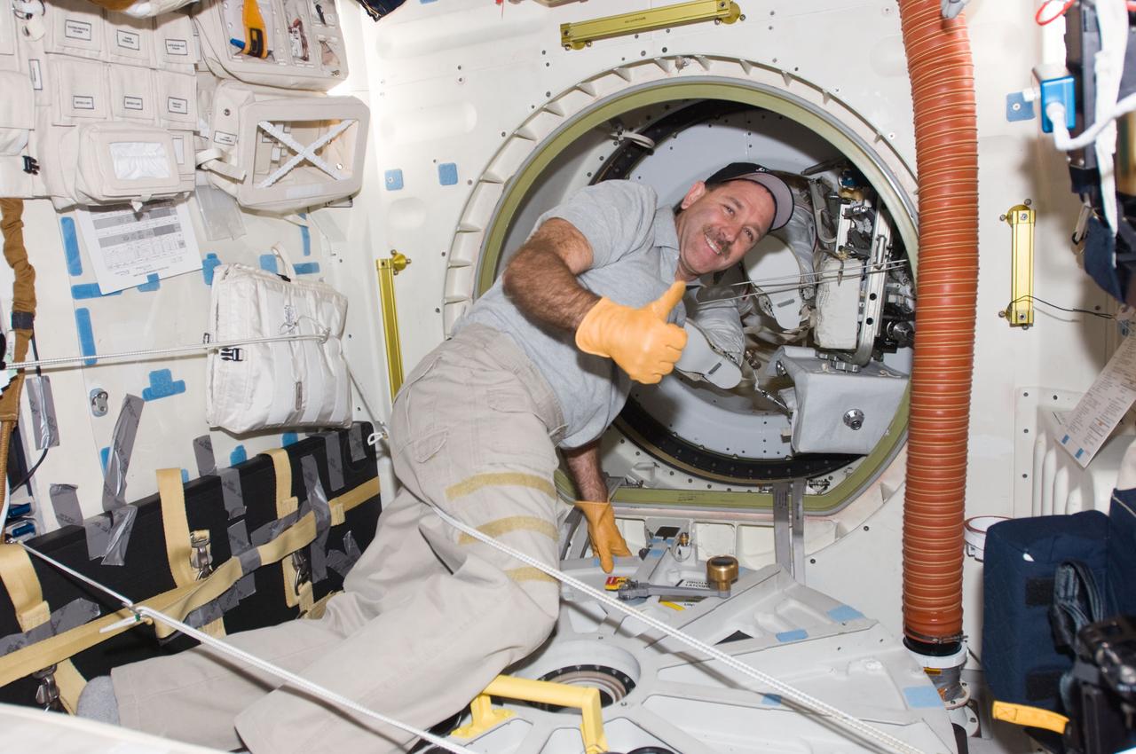 S125-E-007789 (15 May 2009) --- Astronaut John Grunsfeld signals "thumbs up" to indicate two of his crewmates coming inside from a lengthy   space walk are "home."  Grunsfeld had just opened the hatch that leads from the mid deck to the airlock. Completing this day's session of extravehicular activity and in the airlock when this photo was made were astronauts Mike Massimino and Michael Good.