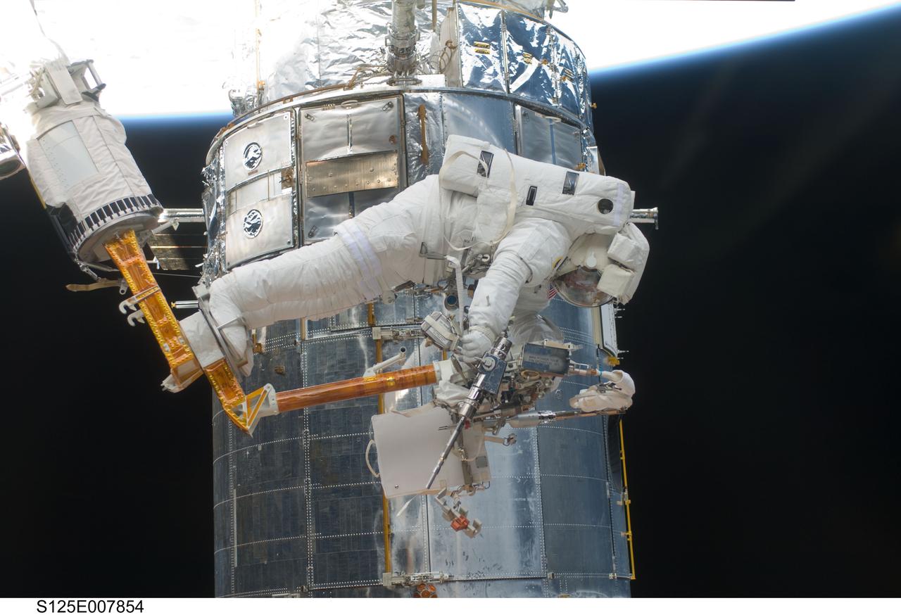 S125-E-007854 (16 May 2009) ---  Astronaut Andrew Feustel, STS-125 mission specialist,  retrieves a power tool as he navigates near the Hubble Space Telescope on the end of the remote manipulator system arm, controlled from inside Atlantis? crew cabin. Astronauts Feustel and John Grunsfeld were continuing servicing work on the giant observatory, locked down in the cargo bay of the  shuttle.