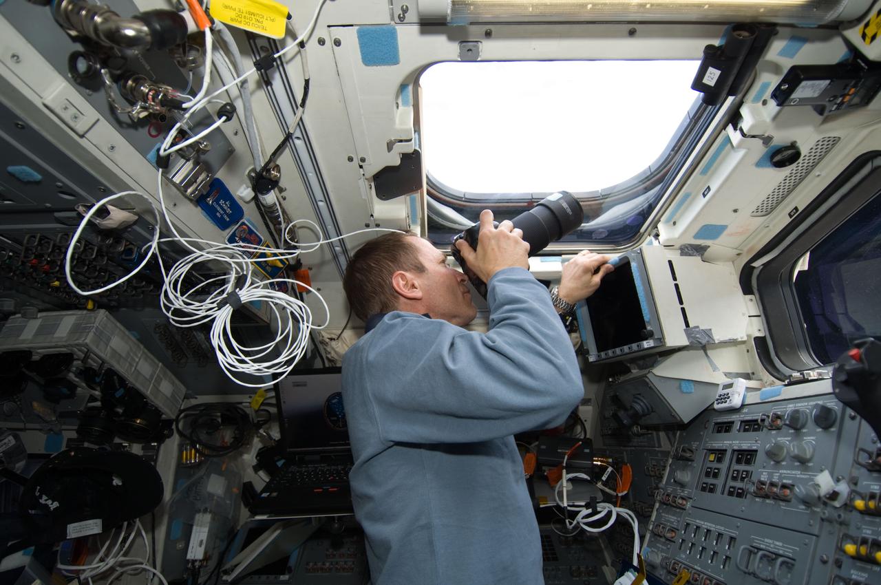 S125-E-008039 (16 May 2009) --- Astronaut Gregory C. Johnson, STS-125 pilot, uses a still camera at an overhead window on the aft flight deck of Space Shuttle Atlantis during flight day six activities.