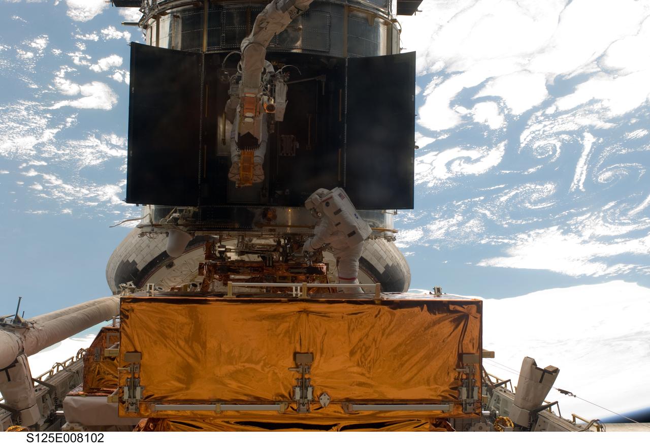 S125-E-008102 (16 May 2009) --- Astronauts Andrew Feustel (partially obscured at top) and John Grunsfeld, both STS-125 mission specialists, participate in the mission?s third session of extravehicular activity (EVA) as work continues to refurbish and upgrade the Hubble Space Telescope. During the six-hour, 36-minute spacewalk, Grunsfeld and Feustel removed the Corrective Optics Space Telescope Axial Replacement and installed in its place the new Cosmic Origins Spectrograph. They also completed the Advanced Camera for Surveys electronic card replacement work, and completed part 2 of the ACS repair, installing a new electronics box and cable.