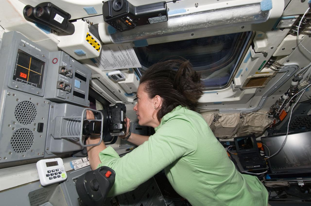 S125-E-009184 (17 May 2009) --- Astronaut Megan McArthur, STS-125 mission specialist, uses a still camera at a window on the aft flight deck of the Earth-orbiting Space Shuttle Atlantis during flight day seven activities.