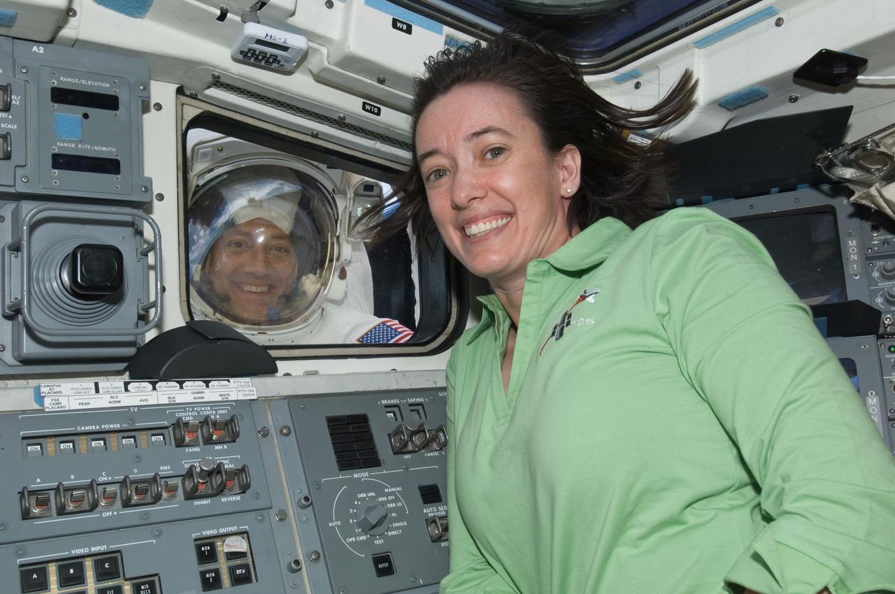 S125-E-009226 (17 May 2009) --- Astronaut Megan McArthur, STS-125 mission specialist, poses for a photo with astronaut Mike Massimino, mission specialist, as he looks through an aft flight deck window of the Earth-orbiting Space Shuttle Atlantis during the mission?s fourth session of extravehicular activity (EVA) as work continues to refurbish and upgrade the Hubble Space Telescope.