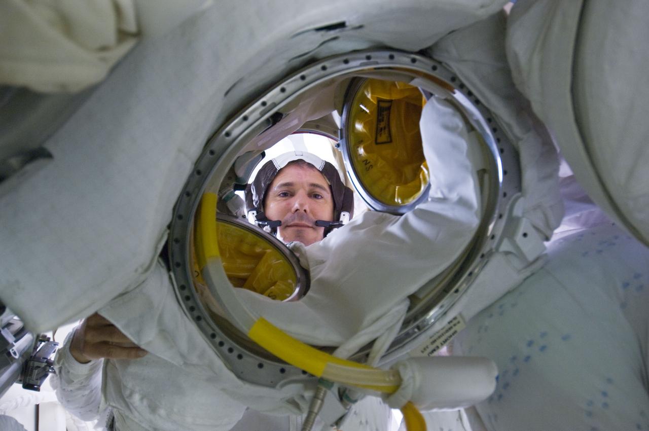 S125-E-009377 (17 May 2009) --- Astronaut Michael Good, STS-125 mission specialist, peers through an opening of his Extravehicular Mobility Unit (EMU) spacesuit on the Earth-orbiting Space Shuttle Atlantis prior to donning it in preparation for the mission?s fourth session of extravehicular activity.