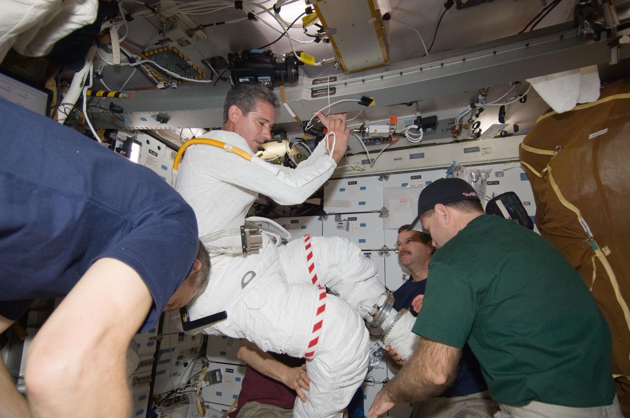 S125-E-009402 (17 May 2009) --- Astronaut Michael Good, STS-125 mission specialist, gets help in the donning of his Extravehicular Mobility Unit (EMU) spacesuit on the middeck of the Earth-orbiting Space Shuttle Atlantis in preparation for the mission?s fourth session of extravehicular activity (EVA). Astronauts John Grunsfeld (right foreground), mission specialist; Scott Altman (right background), commander; and Gregory C. Johnson (background, mostly obscured), pilot, assisted Good. Astronaut Mike Massimino, mission specialist, is at left.