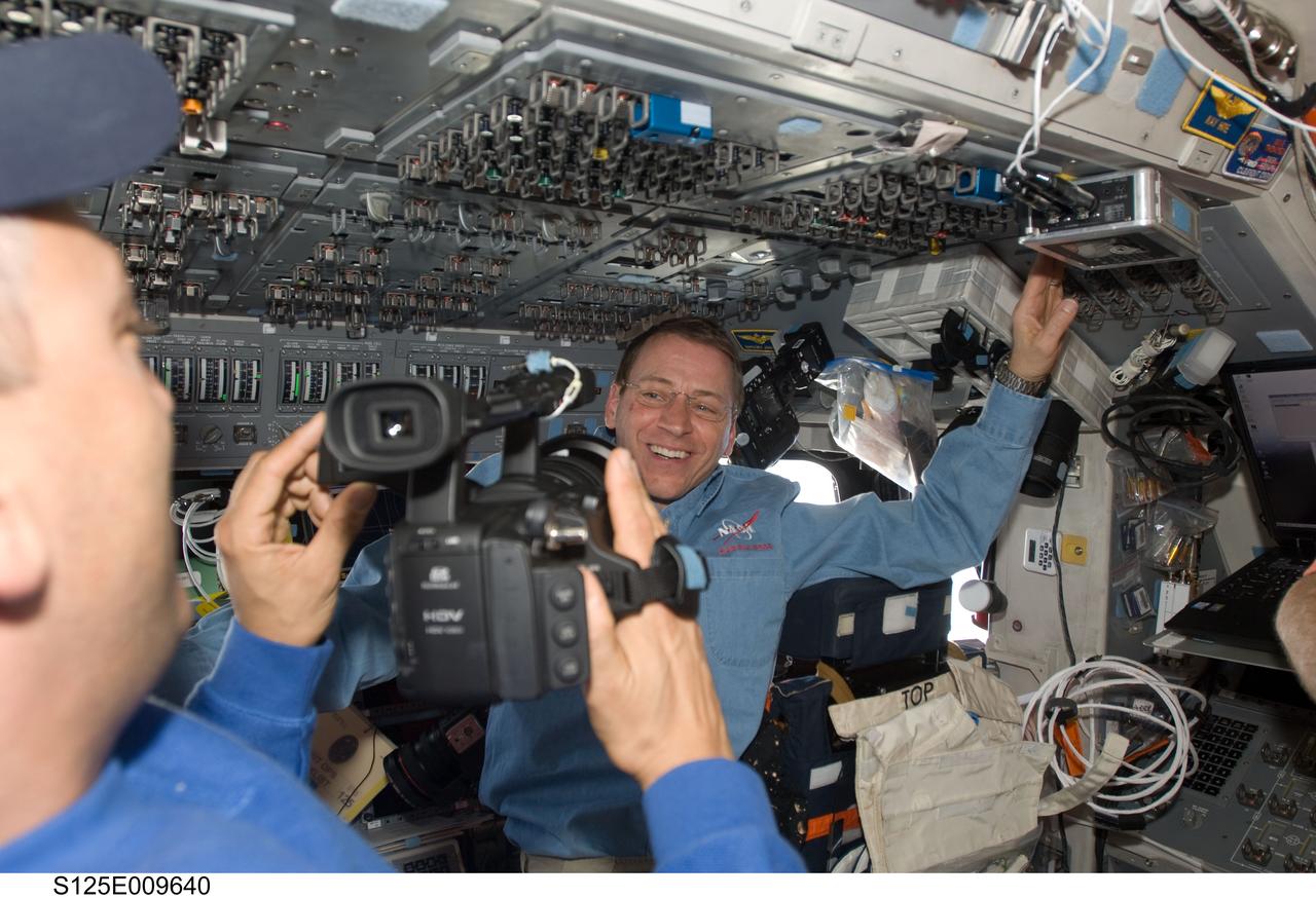 S125-E-009640 (18 May 2009) --- Astronaut Gregory C. Johnson, STS-125 pilot, is photographed by astronaut Mike Massimino (mostly out of frame at left), mission specialist, on the flight deck of the Earth-orbiting Space Shuttle Atlantis during flight day eight activities.