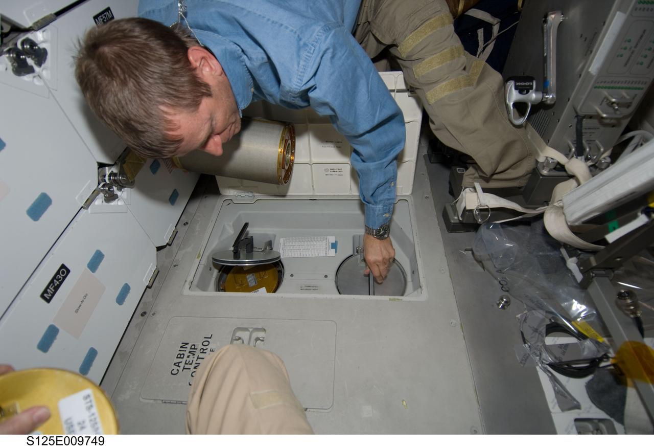 S125-E-009749 (18 May 2009) --- Astronaut Gregory C. Johnson, STS-125 pilot, works with lithium hydroxide (LiOH) canisters from beneath Space Shuttle Atlantis' middeck during flight day eight activities.