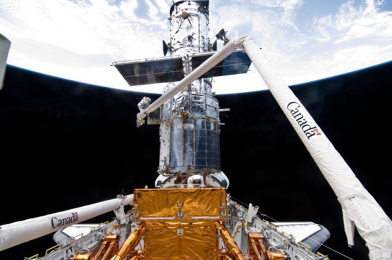 S125-E-009859 (18 May 2009) --- Astronaut John Grunsfeld, STS-125 mission specialist, positioned on a foot restraint on the end of Atlantis? remote manipulator system (RMS), and astronaut Andrew Feustel (bottom center), mission specialist, participate in the mission?s fifth and final session of extravehicular activity (EVA) as work continues to refurbish and upgrade the Hubble Space Telescope. During the seven-hour and two-minute spacewalk, Grunsfeld and Feustel installed a battery group replacement, removed and replaced a Fine Guidance Sensor and three thermal blankets (NOBL) protecting Hubble?s electronics.