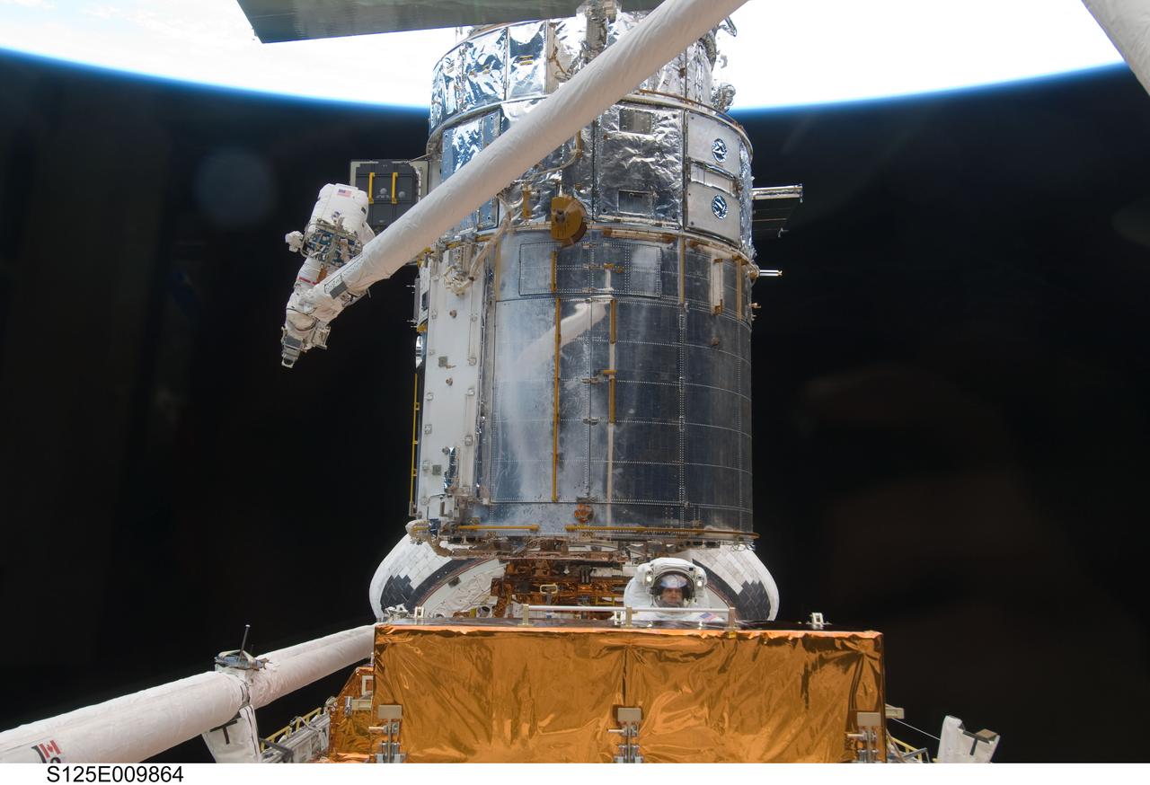 S125-E-009864 (18 May 2009) --- Astronaut John Grunsfeld, STS-125 mission specialist, positioned on a foot restraint on the end of Atlantis? remote manipulator system (RMS), and astronaut Andrew Feustel (bottom center), mission specialist, participate in the mission?s fifth and final session of extravehicular activity (EVA) as work continues to refurbish and upgrade the Hubble Space Telescope. During the seven-hour and two-minute spacewalk, Grunsfeld and Feustel installed a battery group replacement, removed and replaced a Fine Guidance Sensor and three thermal blankets (NOBL) protecting Hubble?s electronics.
