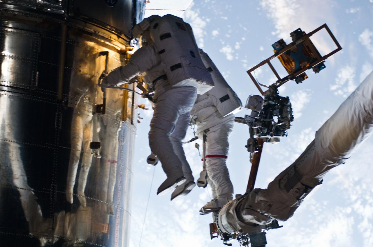 S125-E-009890 (18 May 2009) --- Astronaut John Grunsfeld, STS-125 mission specialist, positioned on a foot restraint on the end of Atlantis? remote manipulator system (RMS), and astronaut Andrew Feustel (foreground), mission specialist, participate in the mission?s fifth and final session of extravehicular activity (EVA) as work continues to refurbish and upgrade the Hubble Space Telescope. During the seven-hour and two-minute spacewalk, Grunsfeld and Feustel installed a battery group replacement, removed and replaced a Fine Guidance Sensor and three thermal blankets (NOBL) protecting Hubble?s electronics.