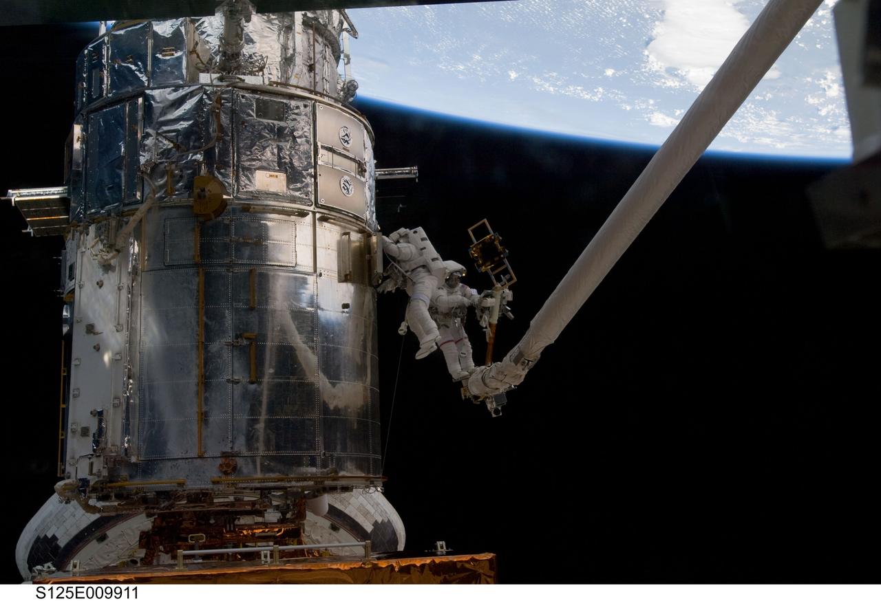 S125-E-009911 (18 May 2009) --- Astronaut John Grunsfeld, STS-125 mission specialist, positioned on a foot restraint on the end of Atlantis? remote manipulator system (RMS), and astronaut Andrew Feustel, mission specialist, participate in the mission?s fifth and final session of extravehicular activity (EVA) as work continues to refurbish and upgrade the Hubble Space Telescope. During the seven-hour and two-minute spacewalk, Grunsfeld and Feustel installed a battery group replacement, removed and replaced a Fine Guidance Sensor and three thermal blankets (NOBL) protecting Hubble?s electronics.
