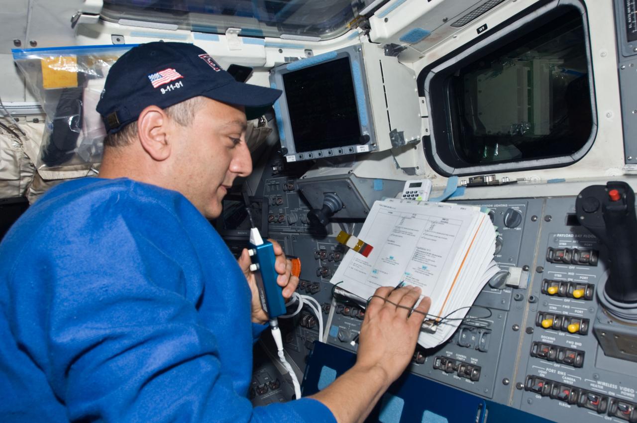 S125-E-009915 (18 May 2009) --- Astronaut Mike Massimino, STS-125 mission specialist, uses a communication system while reading a checklist on the aft flight deck of the Earth-orbiting Space Shuttle Atlantis during flight day eight activities.