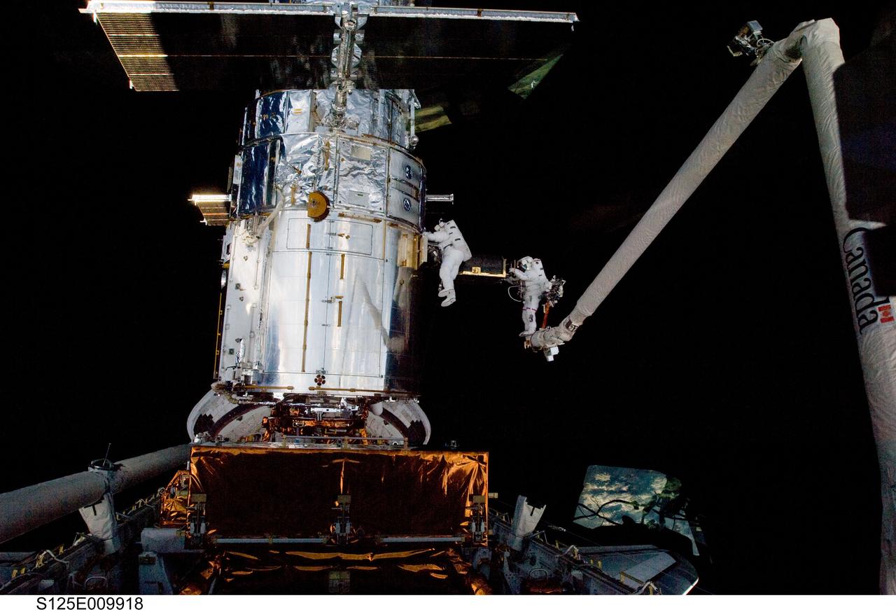 S125-E-009918 (18 May 2009) --- Astronaut John Grunsfeld, STS-125 mission specialist, positioned on a foot restraint on the end of Atlantis? remote manipulator system (RMS), and astronaut Andrew Feustel, mission specialist, participate in the mission?s fifth and final session of extravehicular activity (EVA) as work continues to refurbish and upgrade the Hubble Space Telescope. During the seven-hour and two-minute spacewalk, Grunsfeld and Feustel installed a battery group replacement, removed and replaced a Fine Guidance Sensor and three thermal blankets (NOBL) protecting Hubble?s electronics.