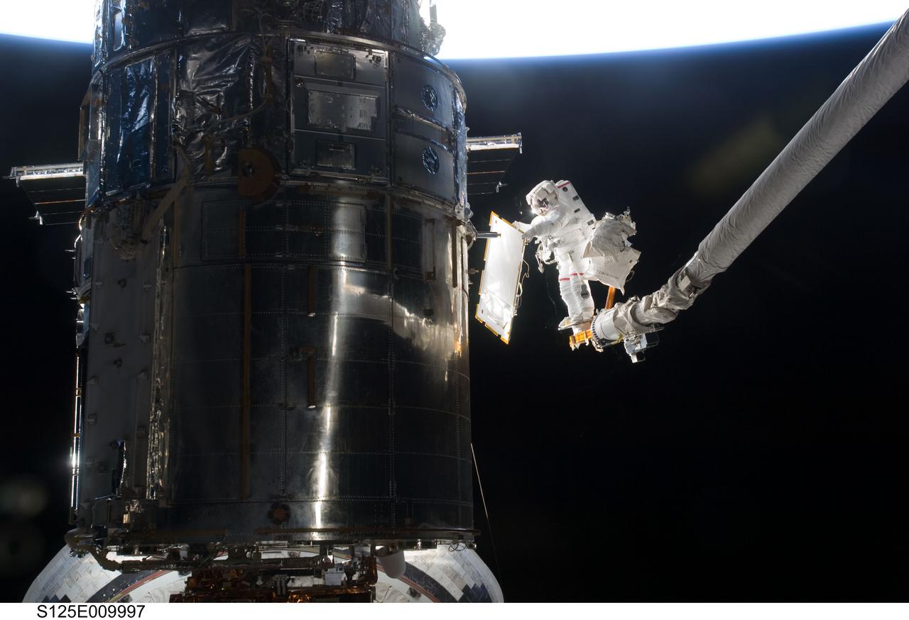 S125-E-009997 (18 May 2009) --- Astronaut John Grunsfeld, STS-125 mission specialist, positioned on a foot restraint on the end of Atlantis? remote manipulator system (RMS), participates in the mission?s fifth and final session of extravehicular activity (EVA) as work continues to refurbish and upgrade the Hubble Space Telescope. During the seven-hour and two-minute spacewalk, Grunsfeld and astronaut Andrew Feustel (out of frame), mission specialist, installed a battery group replacement, removed and replaced a Fine Guidance Sensor and three thermal blankets (NOBL) protecting Hubble?s electronics.