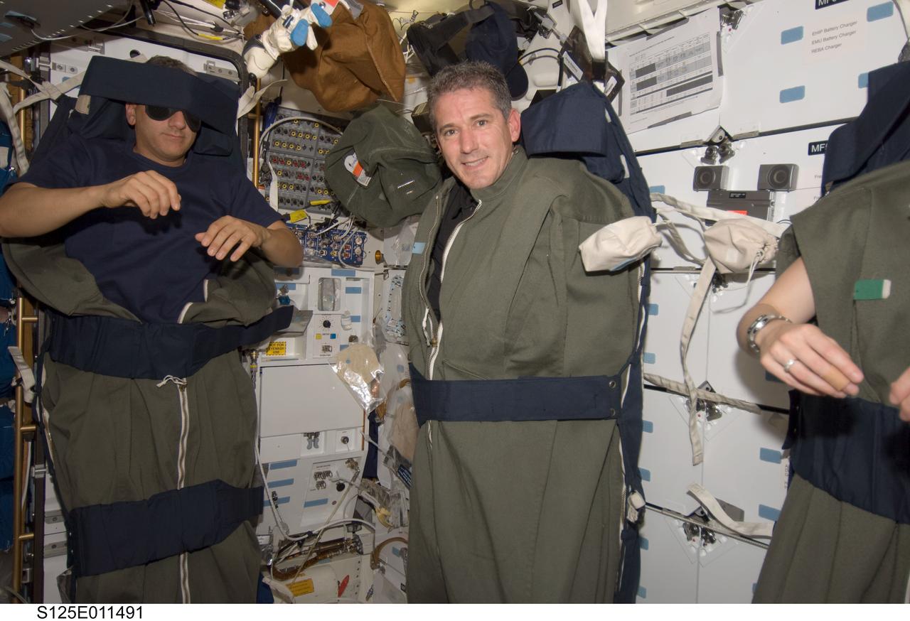 S125-E-011491 (18 May 2009) --- Astronauts Mike Massimino (left), Michael Good and Megan McArthur (mostly out of frame at right), all STS-125 mission specialists, are pictured in their sleeping bags, which are attached to the lockers on the middeck of the Earth-orbiting Space Shuttle Atlantis at the end of flight day eight.