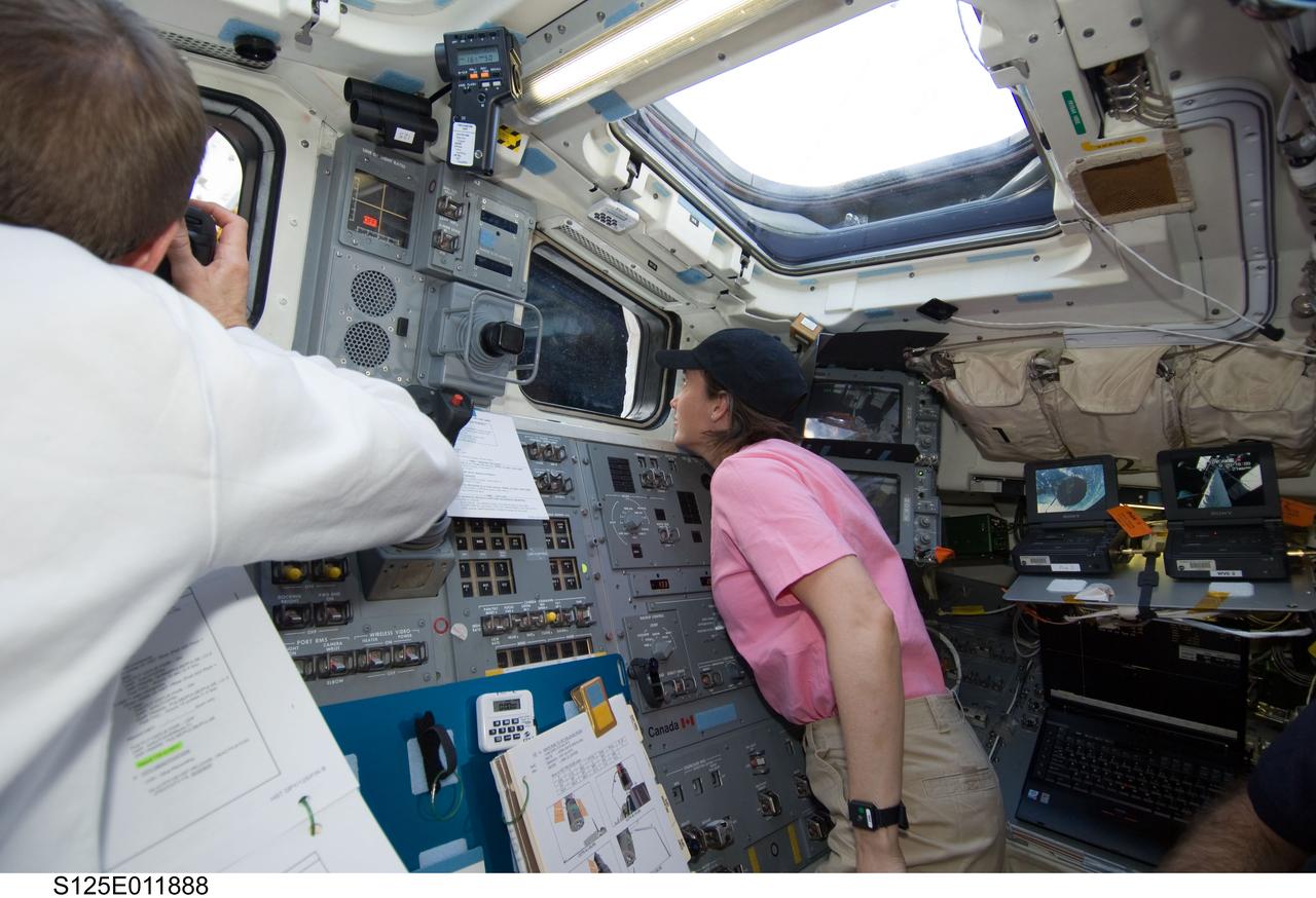 S125-E-011888 (19 May 2009) --- Astronaut Megan McArthur, STS-125 mission specialist, looks through a window on the aft flight deck of the Earth-orbiting Space Shuttle Atlantis during flight day nine activities. Astronaut Gregory C. Johnson (partially out of frame), STS-125 pilot, is at left.