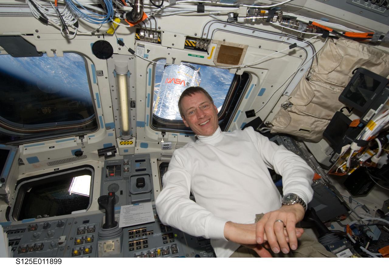 S125-E-011899 (19 May 2009) --- Astronaut Gregory C. Johnson, STS-125 pilot, is pictured on the aft flight deck of the Earth-orbiting Space Shuttle Atlantis during flight day nine activities. A portion of the Hubble Space Telescope and Earth?s horizon are visible through the overhead windows.