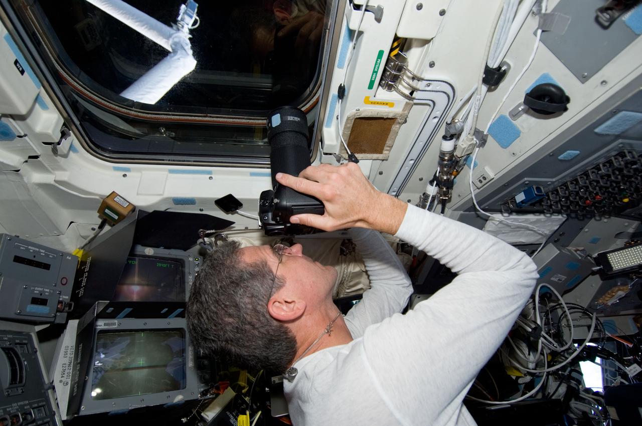 S125-E-011921 (19 May 2009) --- Astronaut Michael Good, STS-125 mission specialist, uses a still camera at an overhead window on the aft flight deck of the Earth-orbiting Space Shuttle Atlantis to photograph the Hubble Space Telescope after its release from Atlantis? remote manipulator system (RMS) robotic arm.