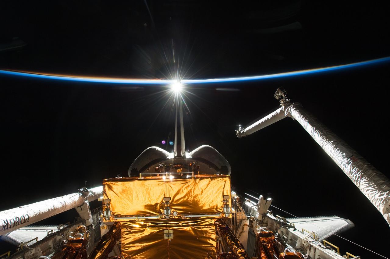 S125-E-012372 (20 May 2009) --- Backdropped by the blackness of space and the thin line of Earth?s atmosphere, Space Shuttle Atlantis? payload bay, Canadian-built remote manipulator system (RMS) robotic arm, vertical stabilizer and orbital maneuvering system (OMS) pods are featured in this image photographed by an STS-125 crewmember on flight day 10.