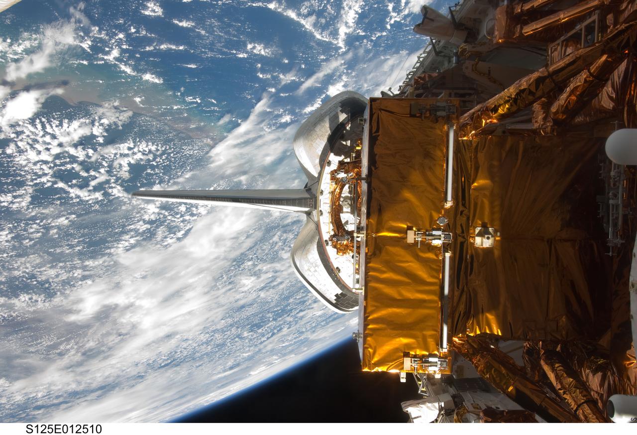 S125-E-012510 (19 May 2009) --- Backdropped by a blue and white Earth, Space Shuttle Atlantis? payload bay, vertical stabilizer and orbital maneuvering system (OMS) pods are featured in this image photographed by an STS-125 crewmember on flight day nine.