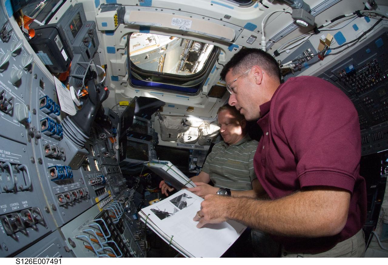 S126-E-007491 (16 Nov. 2008) --- Astronauts Shane Kimbrough (foreground), STS-126 mission specialist; and Eric Boe, pilot, refer to checklists as they work controls on the aft flight deck of Space Shuttle Endeavour during flight day three activities.