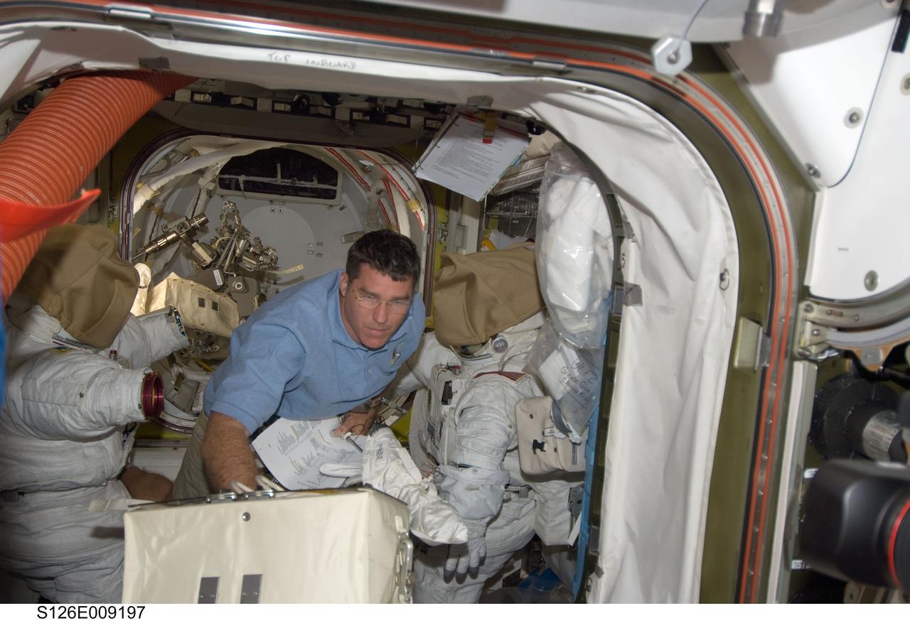 S126-E-009197 (23 Nov. 2008) --- Astronaut Steve Bowen, STS-126 mission specialist, moves a stowage bag in the Quest Airlock of the International Space Station while Space Shuttle Endeavour remains docked with the station.