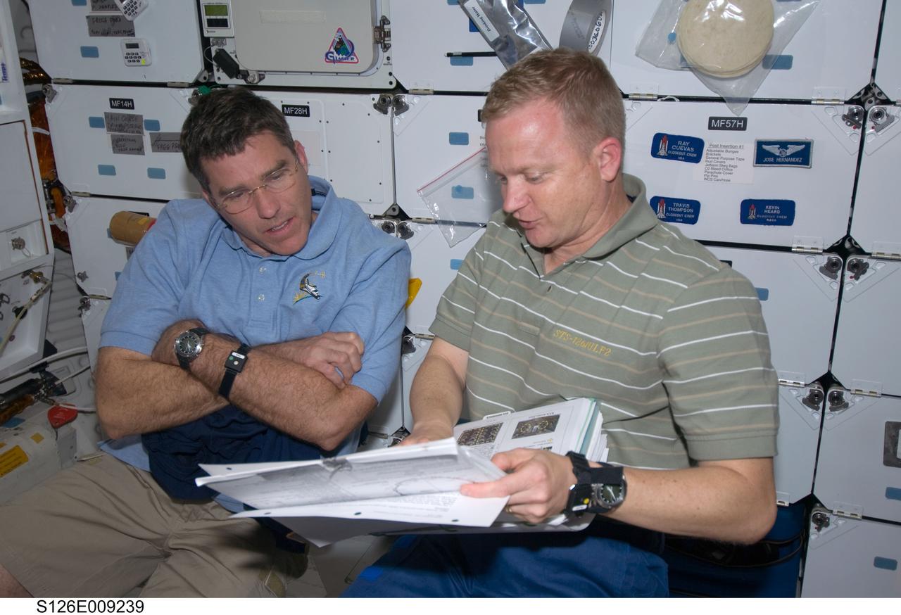 S126-E-009239 (23 Nov. 2008) --- Astronauts Eric Boe (right), STS-126 pilot, and Steve Bowen, mission specialist, look over a procedures manual on the middeck of Space Shuttle Endeavour while docked with the International Space Station.