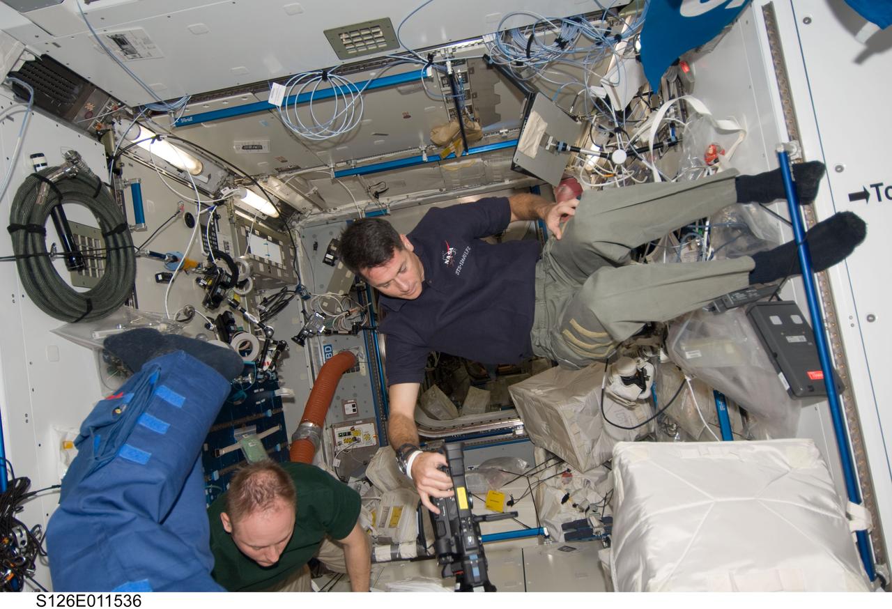 S126-E-011536 (26 Nov. 2008) --- Members of the Space Shuttle Endeavour and International Space Station crews work together in the orbital outpost's Harmony node as they move within a day and half of undocking and going separate ways.  Astronaut Michael Fincke, commander for Expedition 18, is partially visible at lower left. Astronaut Shane Kimbrough, STS-126 pilot, is at right.