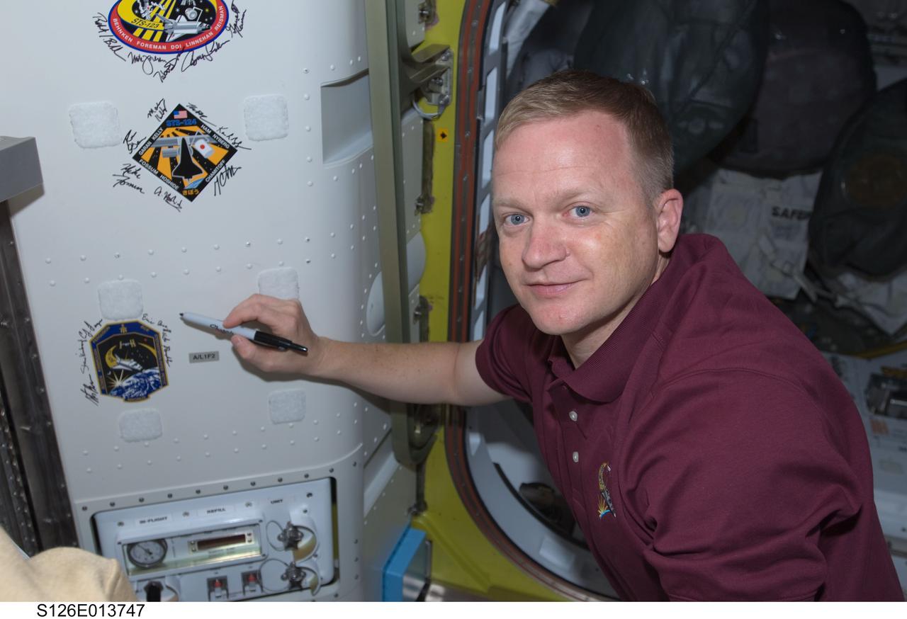 S126-E-013747 (27 Nov. 2008) --- Astronaut  Eric Boe, STS-126 pilot,  signs  Endeavour's crew patch in the Quest Airlock of the International Space Station on Thanksgiving Day.  One more day remains for the Space Shuttle Endeavour to be docked with the station.