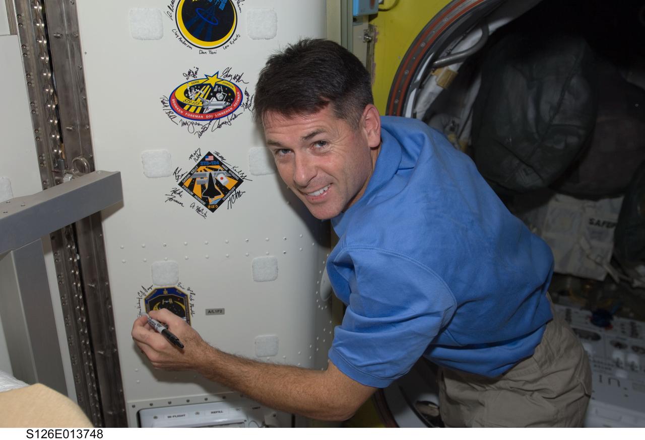 S126-E-013748 (27 Nov. 2008) --- Astronaut Shane Kimbrough, STS-126 mission specialist, signs Endeavour's crew patch in the Quest Airlock of the International Space Station on Thanksgiving Day.  One more day remains for the Space Shuttle Endeavour to be docked with the station.
