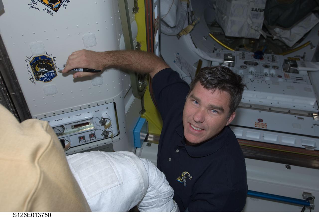 S126-E-013750 (27 Nov. 2008) --- Astronaut Steve Bowen, STS-126 mission specialist, signs Endeavour's crew patch in the Quest Airlock of the International Space Station on Thanksgiving Day. One more day remains for the Space Shuttle Endeavour to be docked with the station.