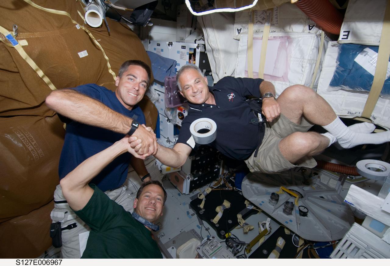 S127-E-006967 (19 July 2009) --- Astronauts Christopher Cassidy (left), Dave Wolf (right)and Tom Marshburn (bottom), all STS-127 mission specialists, share a moment shaking hands with one another on the mid deck of the Space Shuttle Endeavour. Tomorrow Wolf and Marshburn will share more than a few moments performing a spacewalk to perform work on the adjoined International Space Station. Then on flight day 10, Marshburn and Cassidy will perform the fourth of five scheduled space walks.