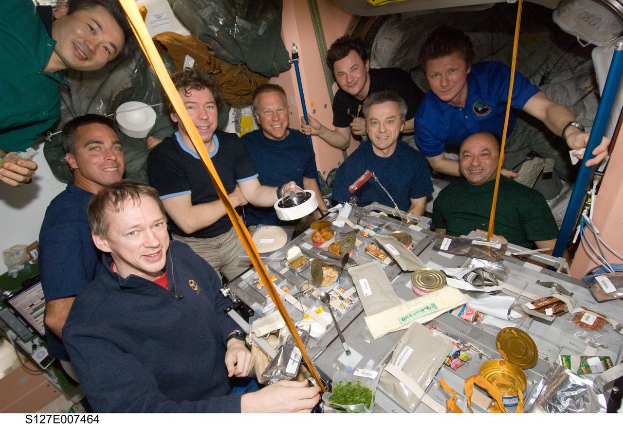 S127-E-007464 (21 July 2009) --- Nine of a total aggregation of 13 astronauts and cosmonauts are pictured at meal time aboard the International Space Station. Seated at the table, clockwise from bottom left, are European Space Agency astronaut Frank De Winne, astronaut Christopher Cassidy, along with astronauts Mike Barratt and Tim Kopra and Canadian Space Agency astronaut Robert Thirsk and astronaut Mark Polansky. From left to right at top are Japanese Aerospace Exploration Agency astronaut Koichi Wakata and Russian Federal Space Agency cosmonauts Roman Romanenko and Gennady Padalka. Not pictured are astronauts Tom Marshburn, Dave Wolf and Doug Hurley, plus Canadian Space Agency astronaut Julie Payette. Barratt is holding a display version of an Apollo 11 lunar sample that had earlier been taken up by a shuttle mission (STS-119) to be onboard the orbital outpost at the time of the current observance of the first moon landing's 40th anniversary. Seven astronauts left Kennedy Space Center one week ago aboard the Space Shuttle Endeavour to join up with the six Expedition 20 crew members on the space station to continue work on it. The space fliers have completed two of five scheduled spacewalks up to this point.