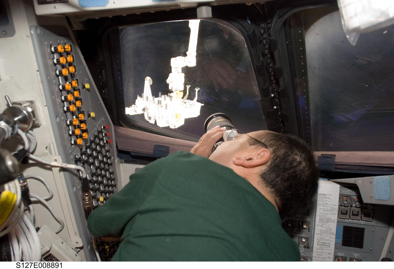 S127-E-008891 (26 July 2009) --- Astronaut Mark Polansky, STS-127 commander, uses a still camera at an overhead window on the aft flight deck of Space Shuttle Endeavour to photograph the Japanese Experiment Module - Exposed Facility in the grasp of the International Space Station’s Canadarm2.