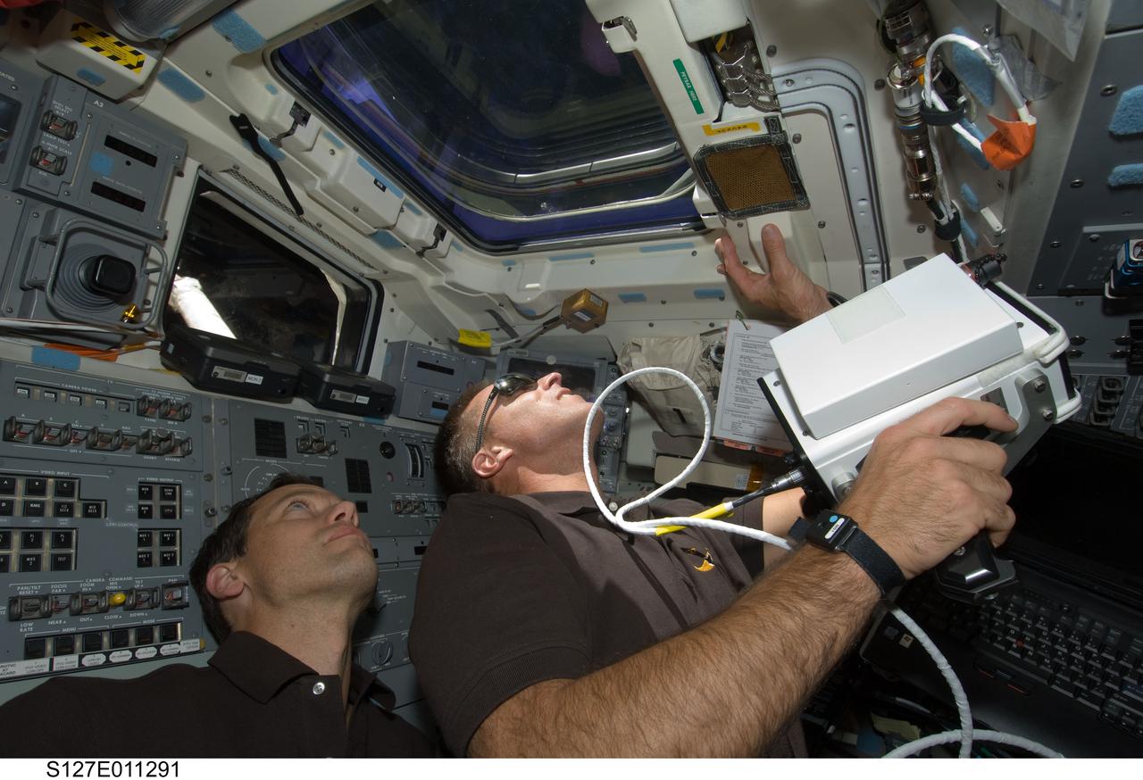 S127-E-011291 (28 July 2009) --- Astronauts Tom Marshburn (left) and Christopher Cassidy, both STS-127 mission specialists, look through an overhead window on the aft flight deck of Space Shuttle Endeavour during flight day 14 activities. Cassidy is holding a handheld laser ranging device -- designed to measure the range between two spacecraft.