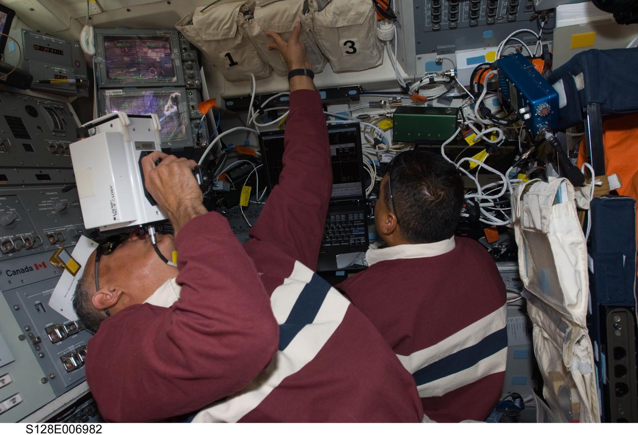 S128-E-006982 (30 Aug. 2009) --- Astronaut John “Danny” Olivas (left), STS-128 mission specialist, uses a handheld laser ranging device at an overhead window on the aft flight deck of the Space Shuttle Discovery to track the range of the International Space Station during rendezvous operations. Astronaut Jose Hernandez, mission specialist, uses a computer at right.