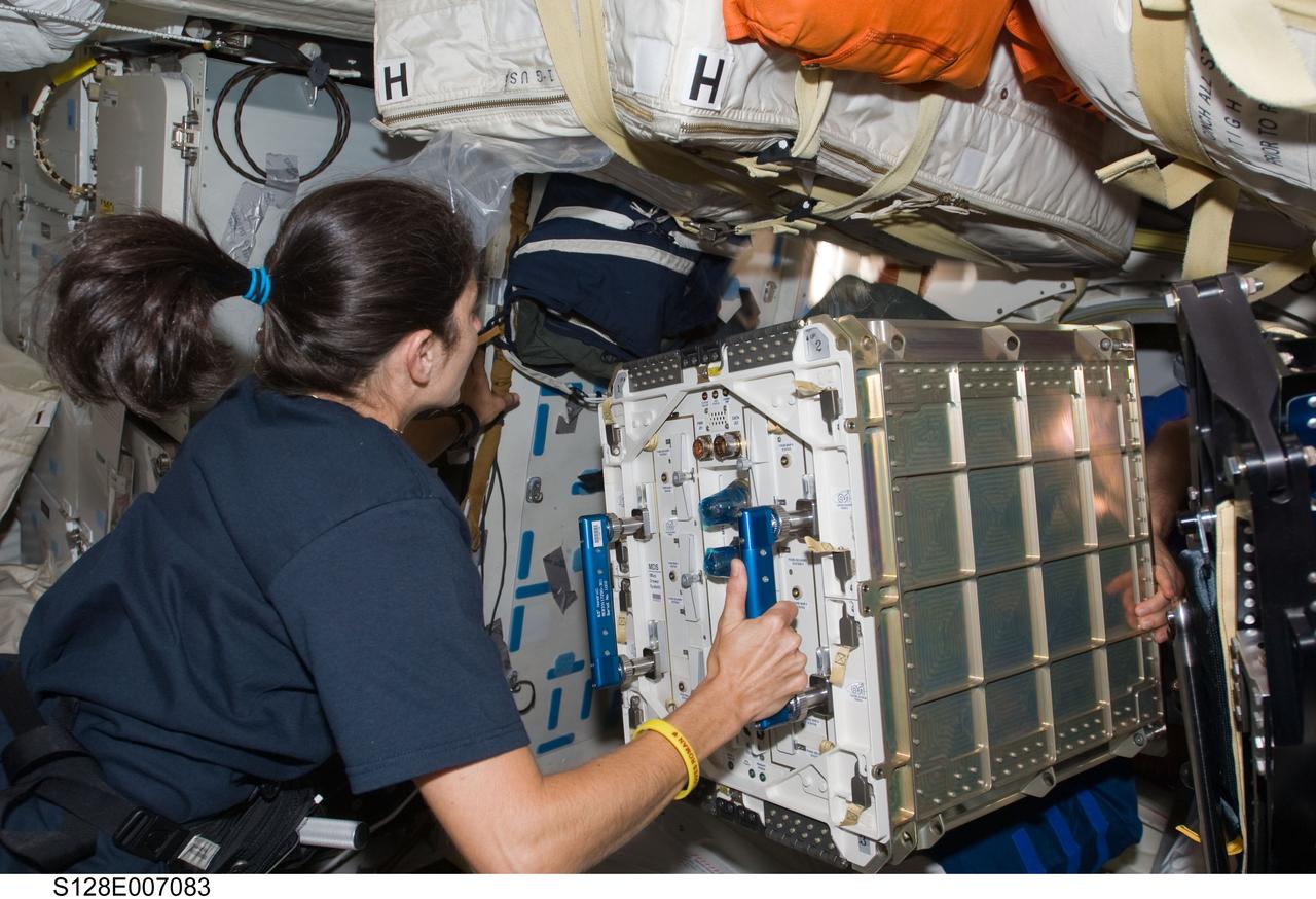 S128-E-007083 (31 Aug. 2009) --- Astronaut Nicole Stott, Expedition 20 flight engineer, prepares to move hardware through a hatch on the middeck of Space Shuttle Discovery (STS-128) while docked with the International Space Station.