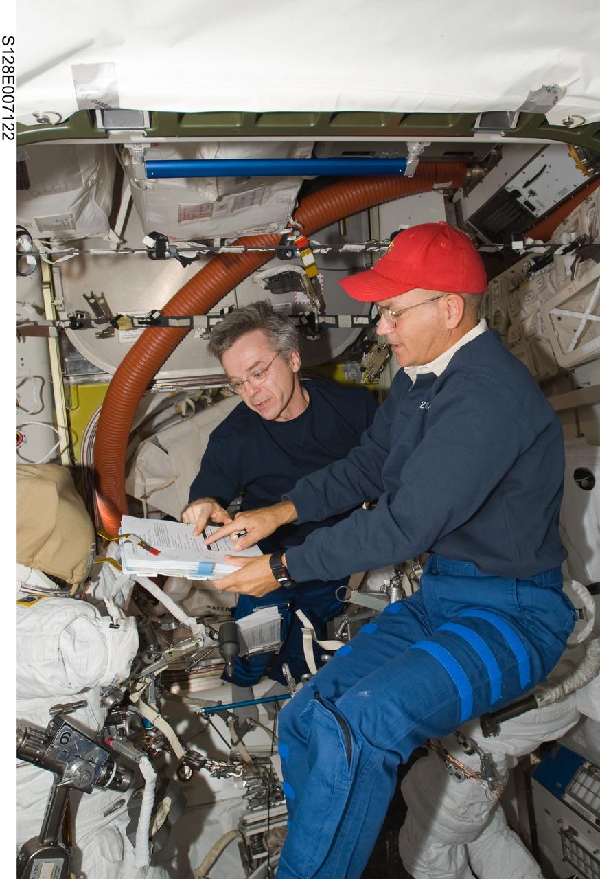 S128-E-007122 (31 Aug. 2009) --- NASA astronaut Rick Sturckow (right), STS-128 commander, and Canadian Space Agency astronaut Robert Thirsk, Expedition 20 flight engineer, look over a checklist in the Quest airlock of the International Space Station while Space Shuttle Discovery remains docked with the station.